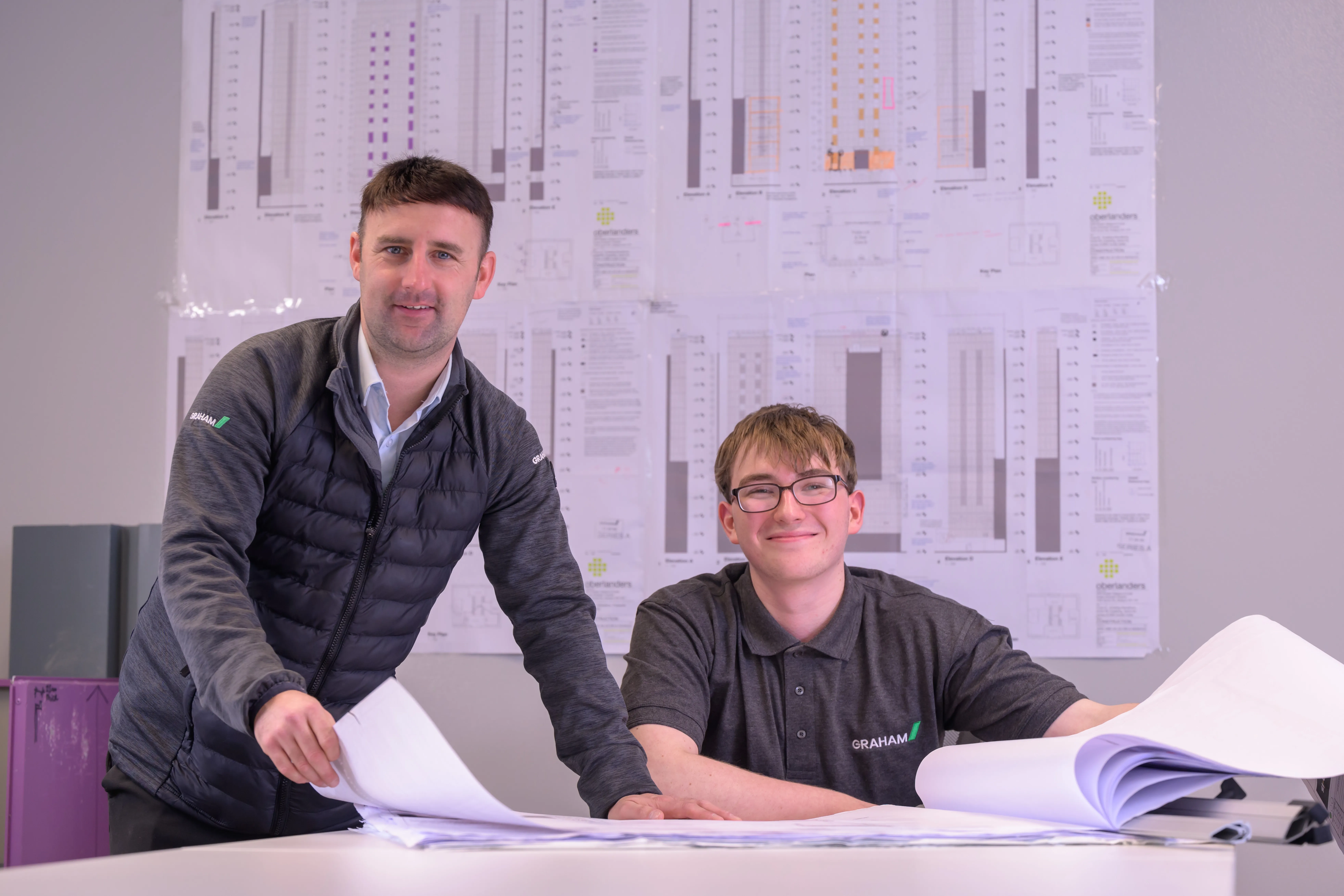 Two smiling men looking at drawings at a desk